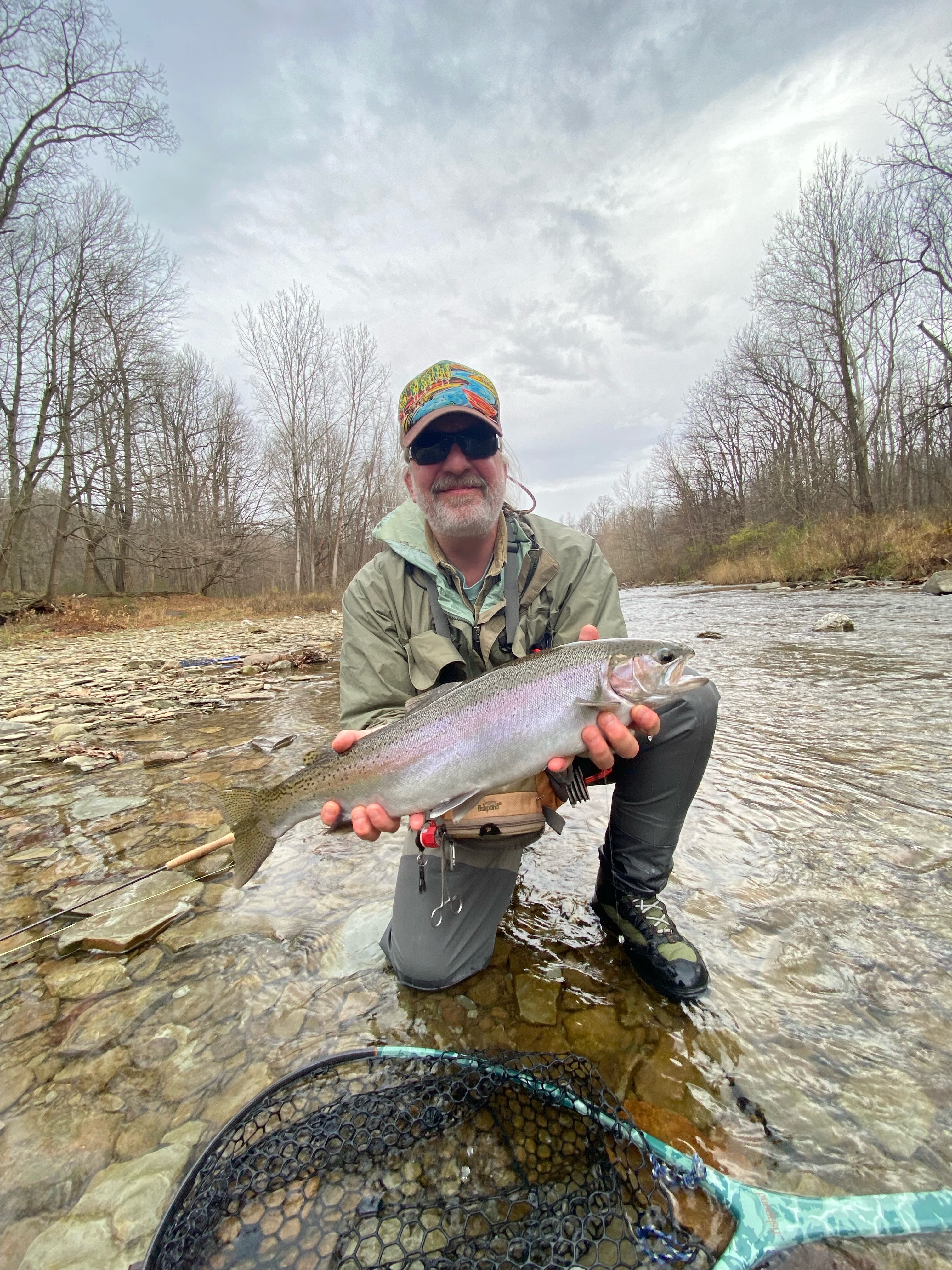 Fisherman standing in a river with fly rod, surrounded by nature
